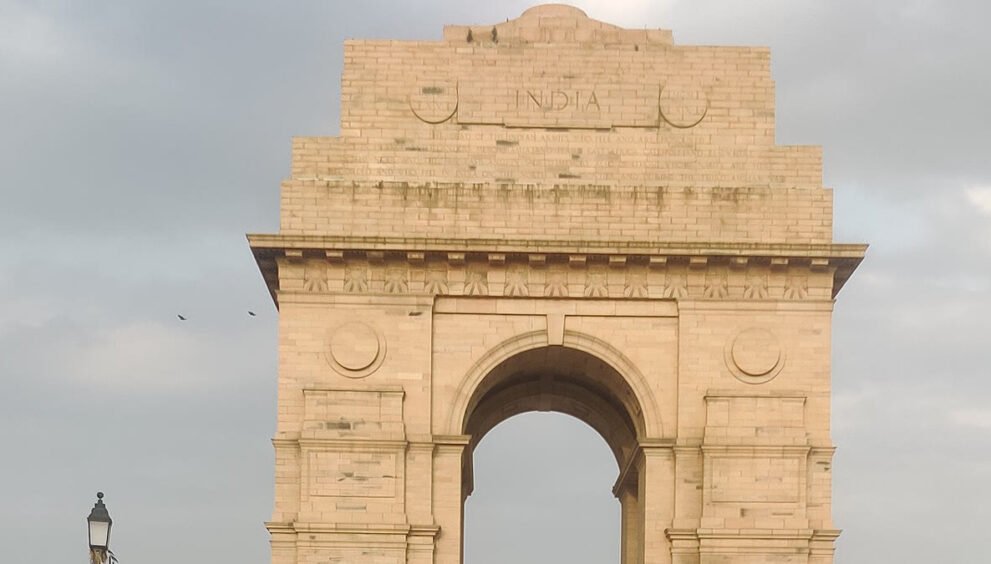 बादलों से घिरे आसमान के नीचे नई दिल्ली का इंडिया गेट और आसपास मौजूद लोग