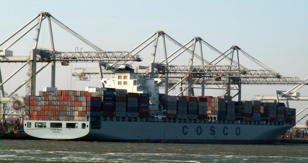 बंदरगाह पर क्रेनों के बीच कंटेनरों से लदा चीनी शिपिंग कंपनी COSCO का मालवाहक जहाज