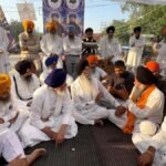 मानसा में परविंदर सिंह झोटा के लिए इंसाफ की मांग पर धरने में बैठे सिख नेता और समर्थक, पीछे झोटा के पोस्टर