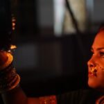 करवा चौथ पर दीये की रोशनी में छलनी थामे सजी-धजी महिला