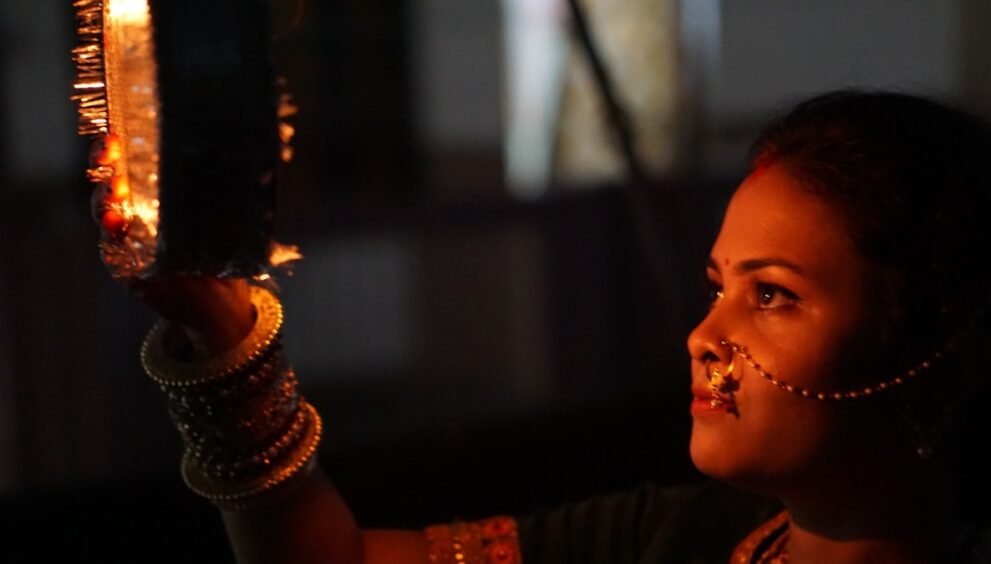 करवा चौथ पर दीये की रोशनी में छलनी थामे सजी-धजी महिला