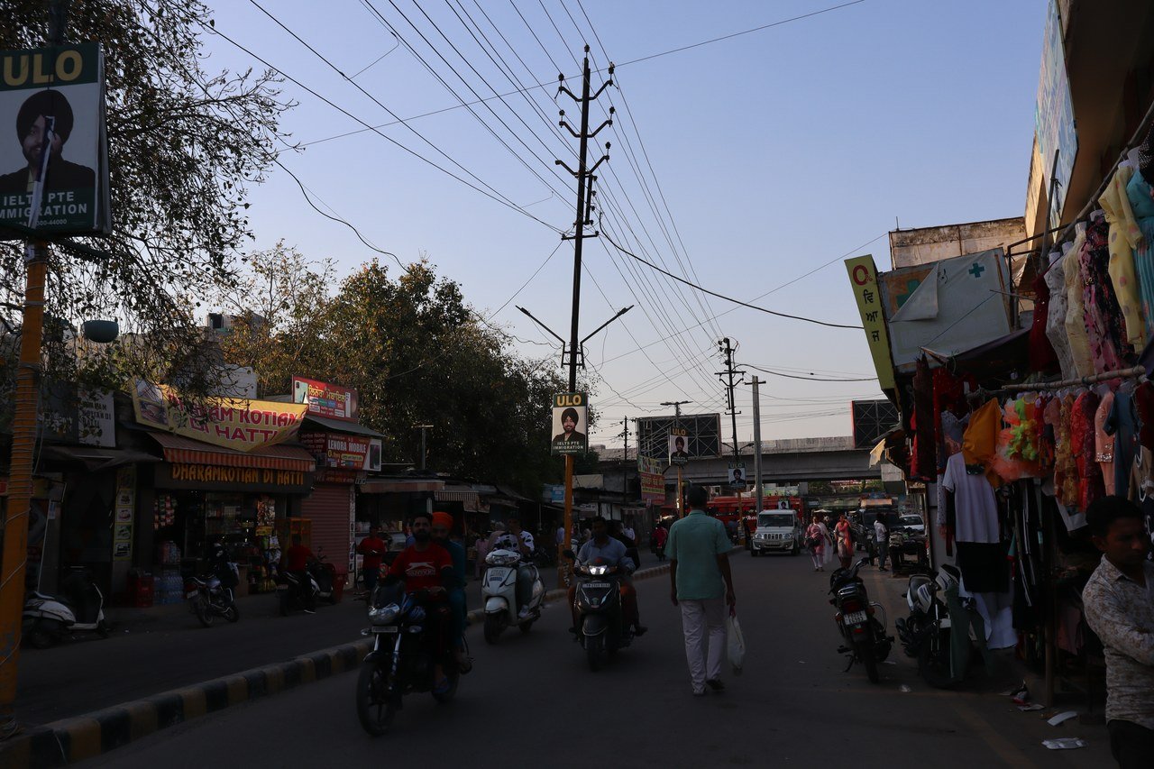 मोगा शहर के एक बाजार की सड़क, किनारे कपड़ों की दुकानें और गुजरते दोपहिया वाहन