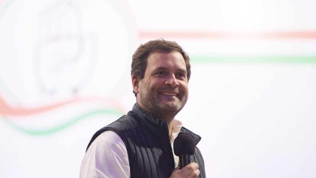 कांग्रेस नेता राहुल गांधी हाथ में माइक लिए मंच पर मुस्कुराते हुए, फाइल फोटो.