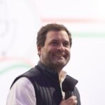 कांग्रेस नेता राहुल गांधी हाथ में माइक लिए मंच पर मुस्कुराते हुए, फाइल फोटो.