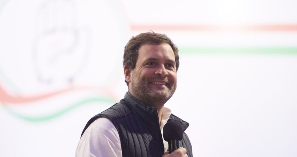 कांग्रेस नेता राहुल गांधी हाथ में माइक लिए मंच पर मुस्कुराते हुए, फाइल फोटो.